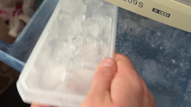 A person pulls out a plastic ice tray filled with ice cubes from the freezer