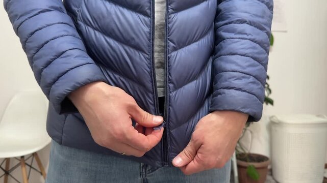 A person zips up a blue puffy jacket