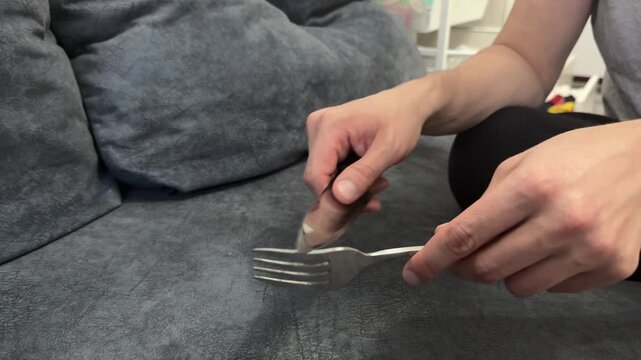 Close-up of hand sliding a knife along metal fork. Sharp metallic sound, gesture of distraction, rhythm or tension in casual indoor environment with soft lighting