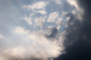 Obraz premium Dramatic sky background with bright sunlit clouds and a dark approaching storm cloud