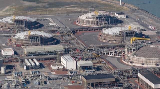 Brugge, Belgium: Aerial view of the Fluxys LNG Terminal Zeebrugge featuring large storage tanks and industrial piping infrastructure under a clear sky.