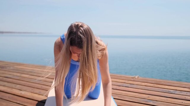 front view of woman performing bird dog yoga pose on mat at wooden pier by sea, focused balance exercise improving core stability strength and coordination, fitness wellness routine outdoor