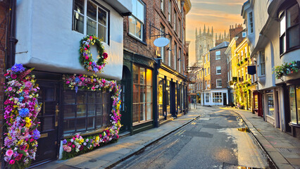 Fototapeta premium View through the Old Town streets of York, England at sunset with flower lined shop facades and York Minster in the background