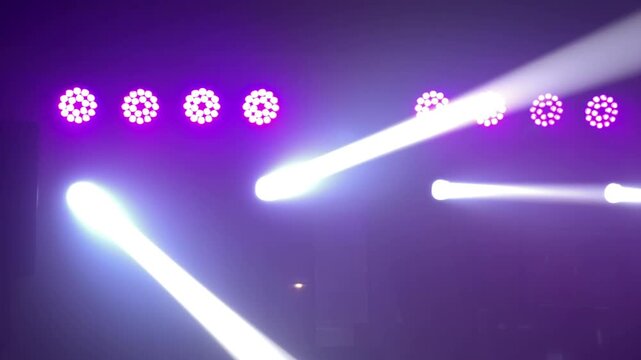 Intense white moving head light beams sweeping through heavy theatrical fog against a backdrop of purple stage lights during a live event.