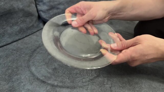 Close-up of fingers rubbing a transparent glass plate to check cleanliness. Home hygiene concept, clean dishes, and daily kitchen routine in soft indoor light