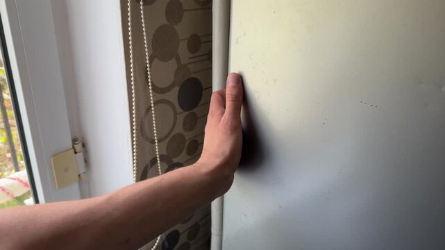 A person gently opens and then closes a refrigerator door, interacting with the metallic surface