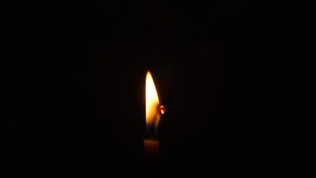 Burning wax candle in complete darkness. A single candle flame in close-up