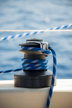Horizontal detail shot of a sailboat's equipment called snatch block, in action with blue and white rope and the sea in the background