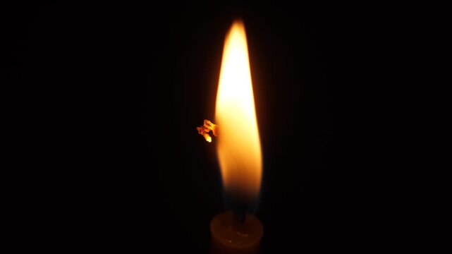 Close-up of a burning candle in complete darkness. A lonely wax candle flame illuminates the gloom