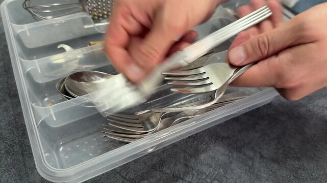 Close up hands placing forks and spoons into plastic drawer organizer in kitchen. Household routine, kitchen organization and storage concept