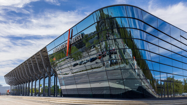 Au&szlig;enansicht des Messezentrums N&uuml;rnberg mit spiegelnder Glasfassade und Schriftzug &bdquo;N&uuml;rnberg Messe&ldquo;. 