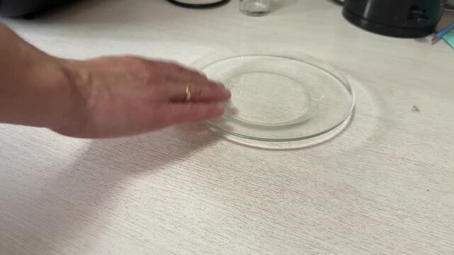 A hand gently slides a clear glass plate across a white table surface