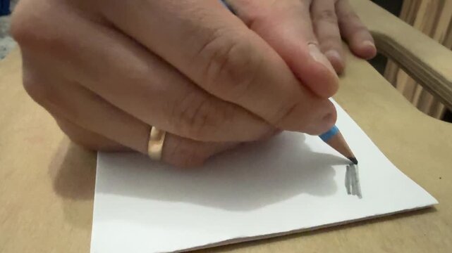 Close-up of hand drawing on a white sheet using a wooden pencil