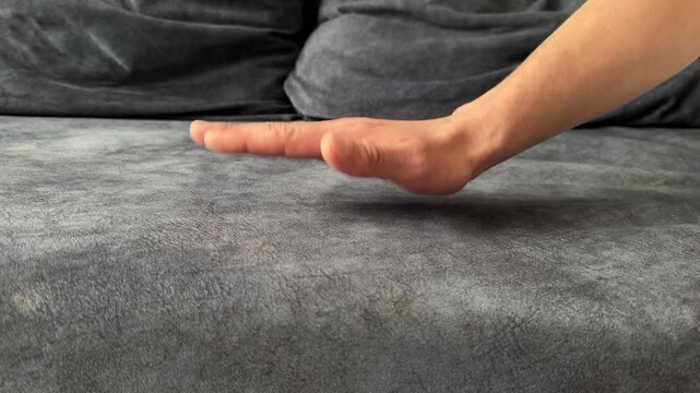 A man taps his hand rhythmically on a soft grey sofa