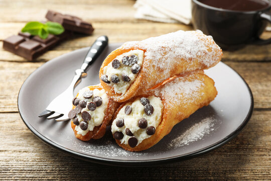 Delicious cannoli with cheese, chocolate, powdered sugar, mint and coffee on wooden table, closeup