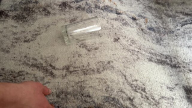 Hand rolling an empty glass across a stone floor surface