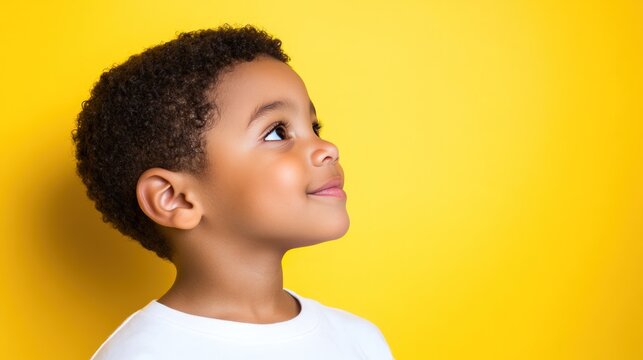 Young boy looking up with a smile against a vibrant yellow background