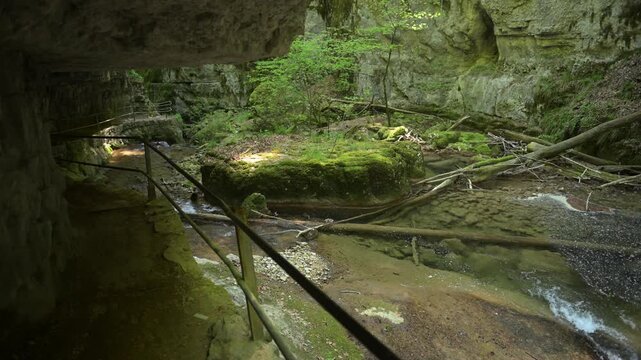Twannbach Gorge, Switzerland - Rocky ravine with shallow creek, moss-covered stones, and a narrow walkway under a natural rock overhang in a green forest setting.