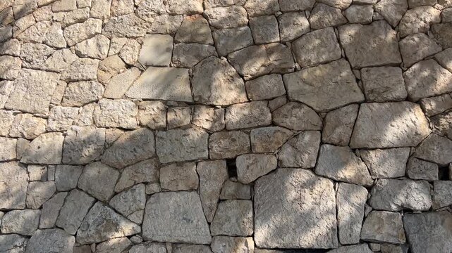 Textured Stone Wall: A close-up shot revealing a sturdy stone wall, the rough-hewn texture of the stones, illuminated by the play of light and shadow, tells a tale of age and enduring strength.