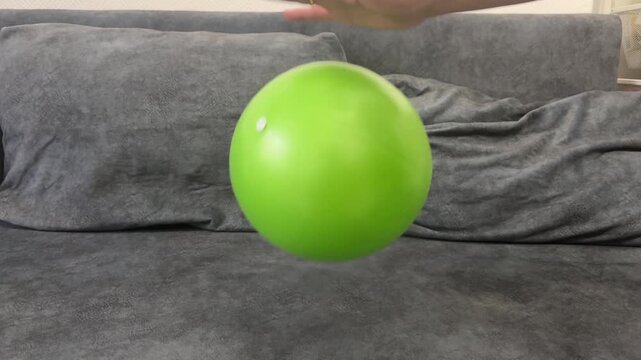 Hand rhythmically tapping green fitness ball, making it bounce. Indoor activity for health or stress relief.