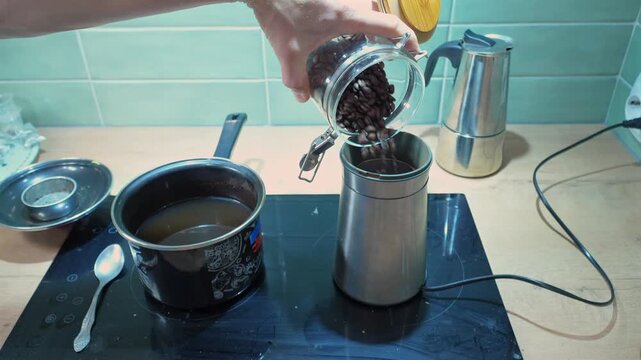 male hands pouring coffee beans into grinder close-up, kitchen preparation process with adding beans and grinding coffee, making fresh drink, action of processing beans for brewing at home