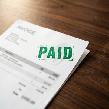 Single paper invoice with green PAID stamp on dark wood surface