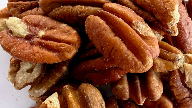 A dense cluster of pecan nut kernels fills the frame with rich brown tones. Wrinkled surfaces and natural breaks create detailed organic texture and depth