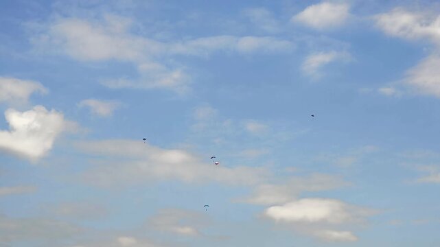 Group of skydivers with parachutes open, descending through a beautiful blue sky with scattered white clouds on a sunny day