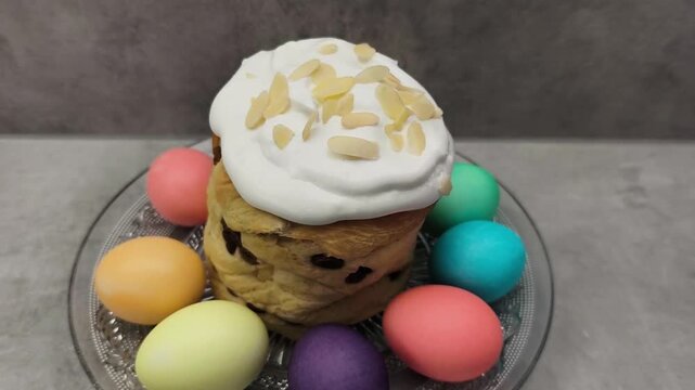 Delicious easter bread decorated with white icing and almond flakes. Colorful dyed eggs surround the traditional sweet cake on a glass plate