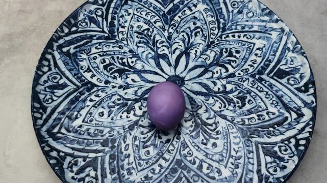 Colorful purple easter egg spinning on a beautiful blue and white ornamental ceramic plate. Festive holiday decoration for a happy easter celebration