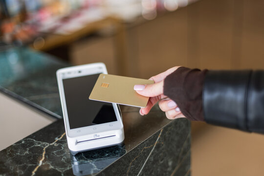 A customer makes a wireless transaction using a gold credit card over a smart payment reader at a store counter. Highlighting NFC technology, secure banking, and easy shopping experiences.