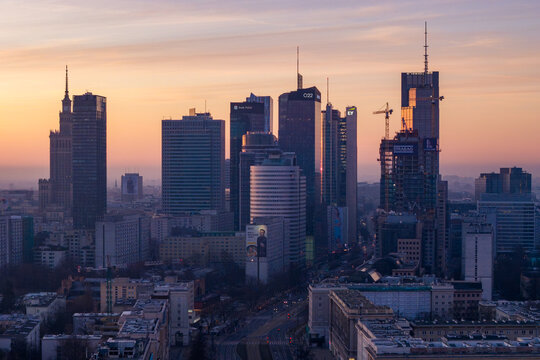 Warsaw, Poland - 05 March 2026: Aerial view of the city skyline featuring modern skyscrapers and the Palace of Culture and Science under a warm sunset sky.
