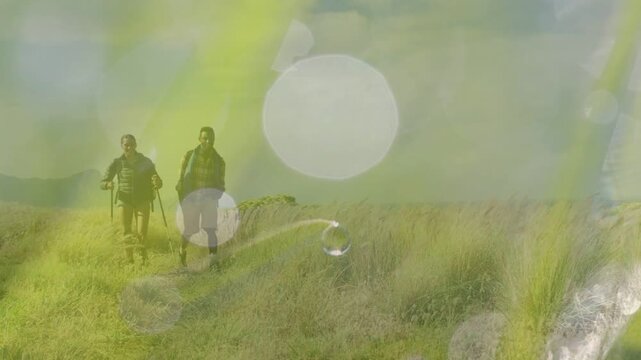 Two hikers walking narrow meadow path drawing them forward, bokeh overlay drifting over duo
