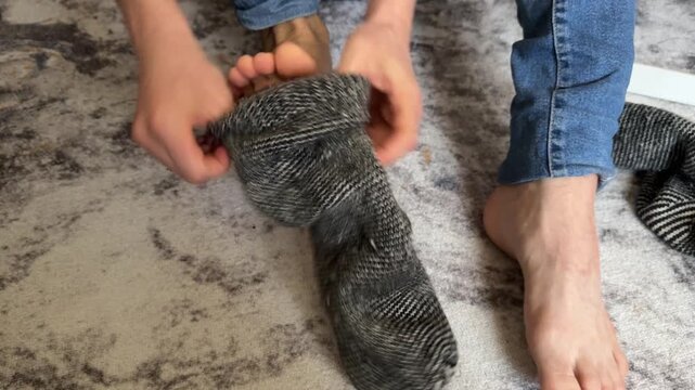 A person puts on a thick wool sock while seated on the floor