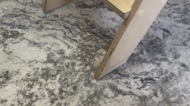 Person sliding a wooden folding step stool across a patterned floor. Indoor movement scene, concept of furniture repositioning, DIY tasks or household adjustments