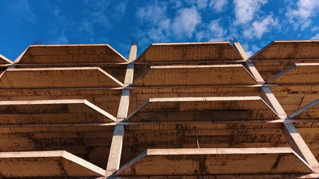 Low angle view of concrete balconies on unfinished building. Bottom-up perspective of unfinished concrete floors and balconies of a building frame against clear blue sky.