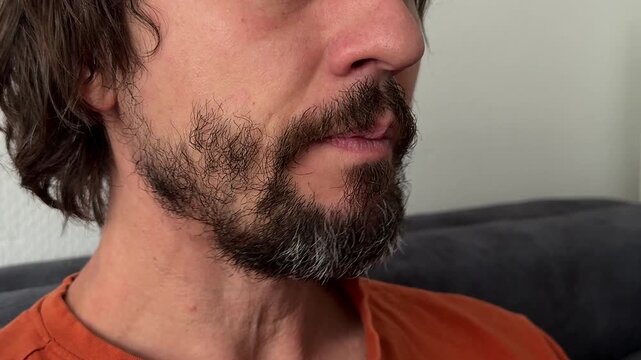 Man makes a chewing motion with lips closed and jaw moving. Beard and mustache visible. Calm indoor expression suggesting eating, habit, or reflex action