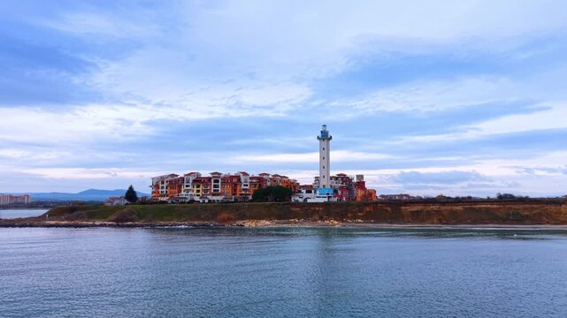 Panoramic view of lighthouse and resort on coastal cliff. Wide aerial perspective of a lighthouse and residential buildings situated on a cliff above the sea.