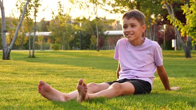 Happy child boy relaxing on grass at sunset in park, enjoying carefree childhood and freedom. Warm sunlight creates peaceful outdoor atmosphere, concept of summer lifestyle, happiness and wellbeing