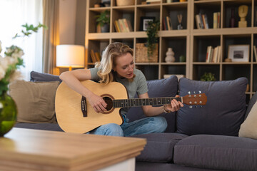 Obraz premium Woman playing acoustic guitar and singing on sofa