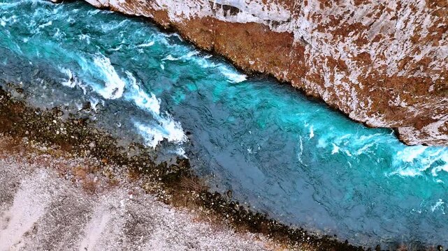 Top down aerial view of turquoise river rapids. Close-up drone shot of turquoise water rapids and rocky bank in Piva river canyon during autumn season.