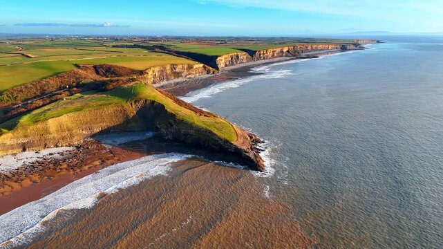 Aerial view of rocky headland and muddy coastal water. Coastal headland with green grass and steep cliffs overlooking ocean with sedimented brown water near the shore.