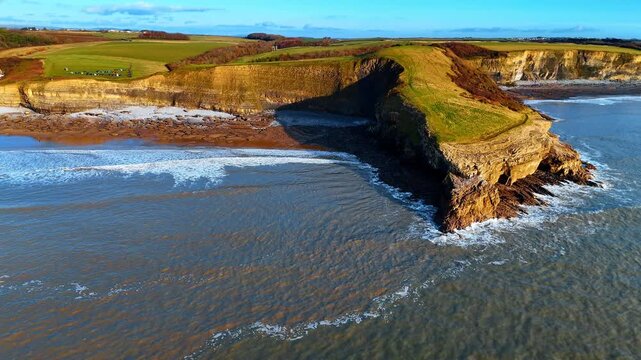 Side view of Witches Point headland and cliffs at Southerndown. Aerial shot showing the steep limestone cliffs and rocky shoreline of the Heritage Coast in South Wales.