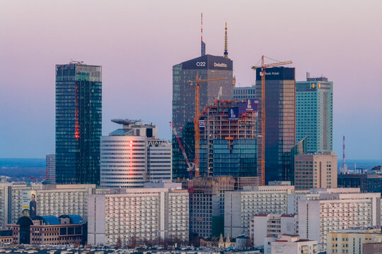 Warsaw, Poland - 21 March 2026: Aerial view of modern skyscrapers and construction cranes against a soft pink dusk sky in the city center.