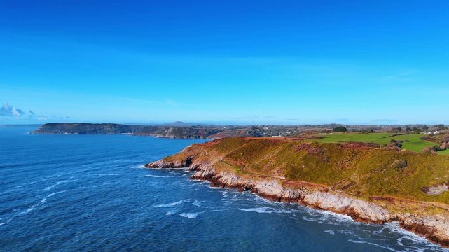 Aerial view of Gower Peninsula coastline and blue sea Wales. High angle drone shot of rocky cliffs coastal path and blue ocean water under clear sky in Wales UK