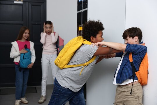 Bullying. Boy fighting with his African American classmate in school