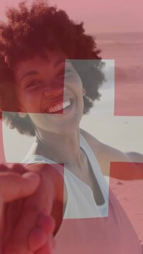 Vertical video: Woman reaching, guiding phone-holder along beach, Swiss flag overlay framing travel