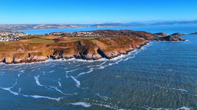 Aerial view of Mumbles headland and Swansea bay Wales. Wide drone shot of coastal town green hills and rocky islands in Bristol Channel Wales UK