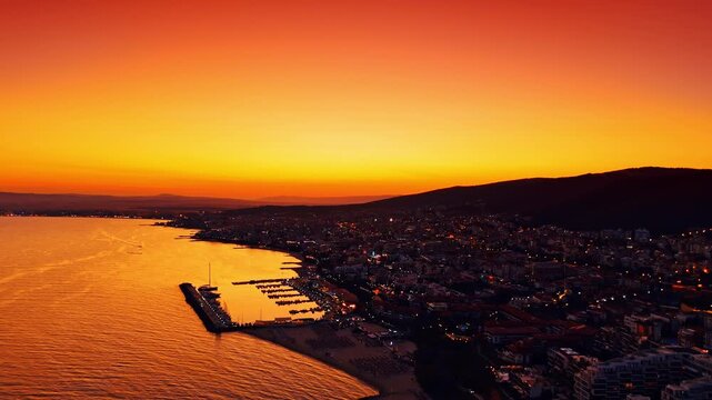 Resort city on the mountainous sea shore switches on lights. Drone footage near the coast at sunset.