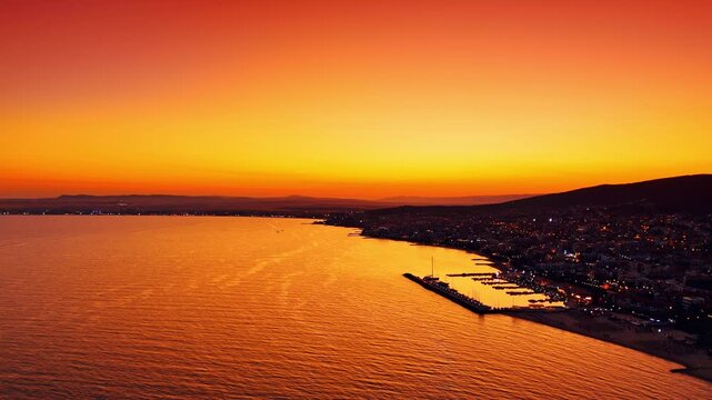 Amazing sunset over the seascape. Flying towards the rocky shore covered with lively modern resort cityscape.